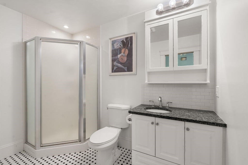 Bathroom with glass shower, dark stone vanity countertop, mirrored cabinet, and black-and-white patterned tile floor.
