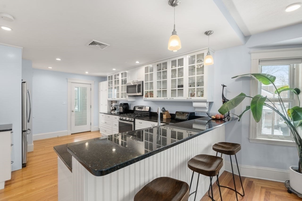 Kitchen with a large granite island, white glass-front cabinets, stainless steel appliances, and hardwood floors.