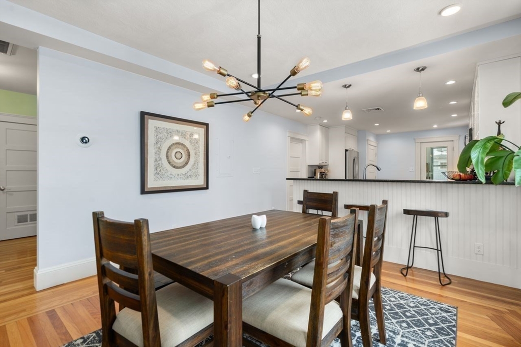Dining area with a dark wood table, hardwood floors, and an open kitchen with breakfast bar.