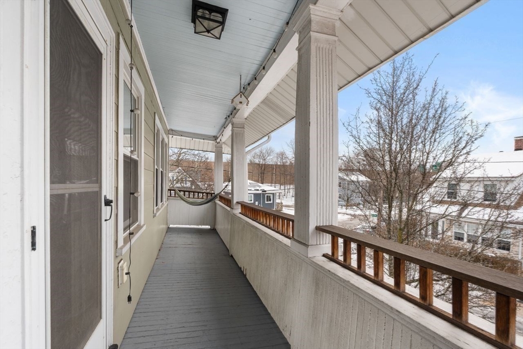 Covered porch with white columns, wooden railing, and a hammock overlooking snow-covered homes.