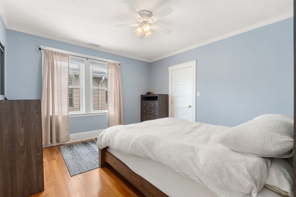 Bedroom with a white bed, light blue walls, hardwood floors, and two curtained windows.