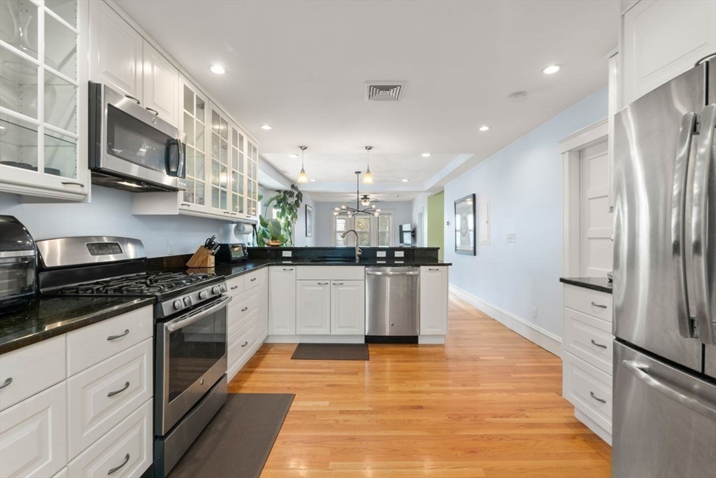 Kitchen with white cabinets, black countertops, stainless steel appliances, and warm hardwood floors.