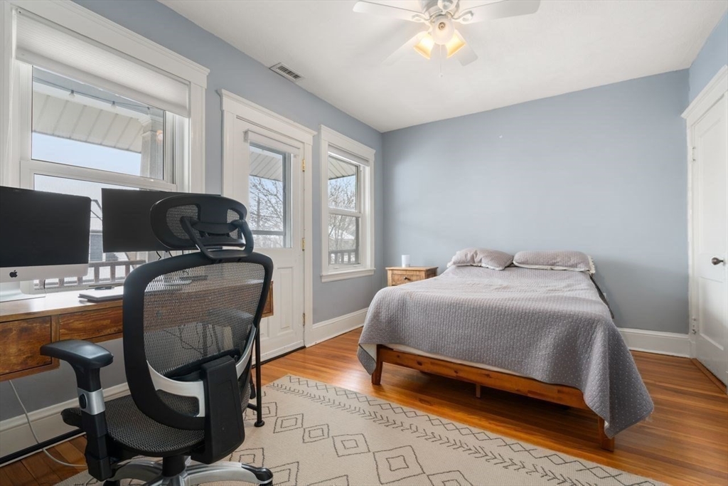 Bedroom with a gray bed, wood floors, and a desk beside tall windows.