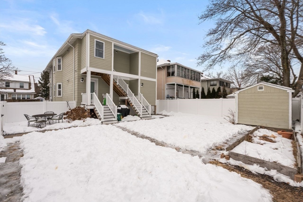 Two-story home with white exterior stairs and a snow-covered fenced backyard.