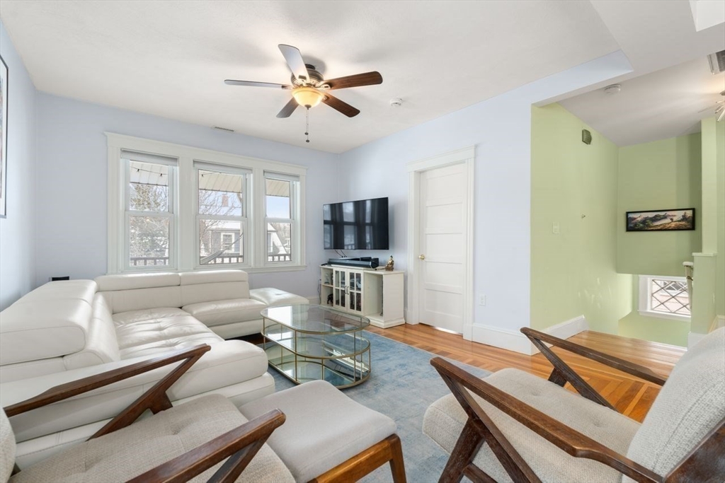 Living room with a white sectional, wood-framed chairs, glass coffee table, and three bright windows.
