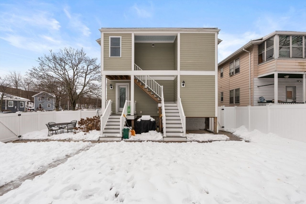 Beige two-story house with exterior staircases and a snow-covered fenced yard.