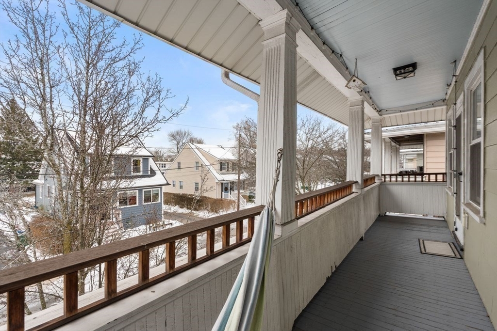 Covered porch with white columns and wood railing overlooking a snowy residential street.
