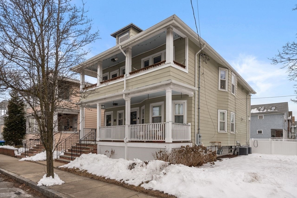 Two-story beige home with stacked covered porches and snow along the sidewalk.