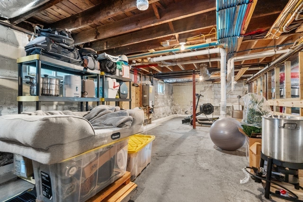 Unfinished basement with exposed joists, storage shelves, plastic bins, and exercise equipment.