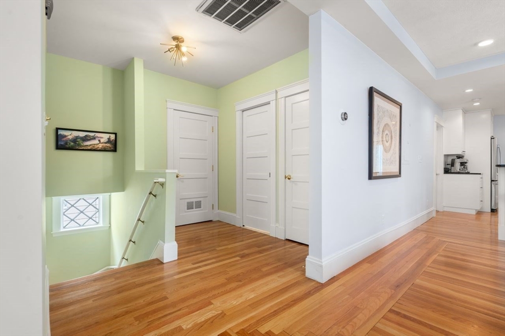 Bright hallway with hardwood floors, pale green walls, white paneled doors, and stairs.