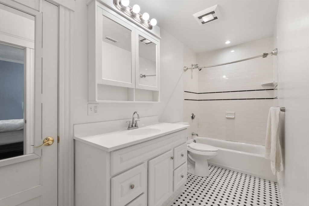 White bathroom with a long vanity, tiled tub and shower, and black-and-white patterned floor.