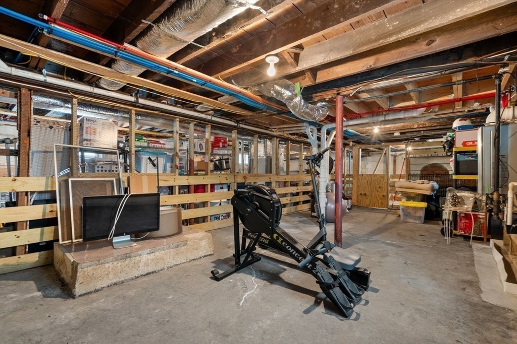 Unfinished basement with exposed joists, storage shelves, and a rowing machine.