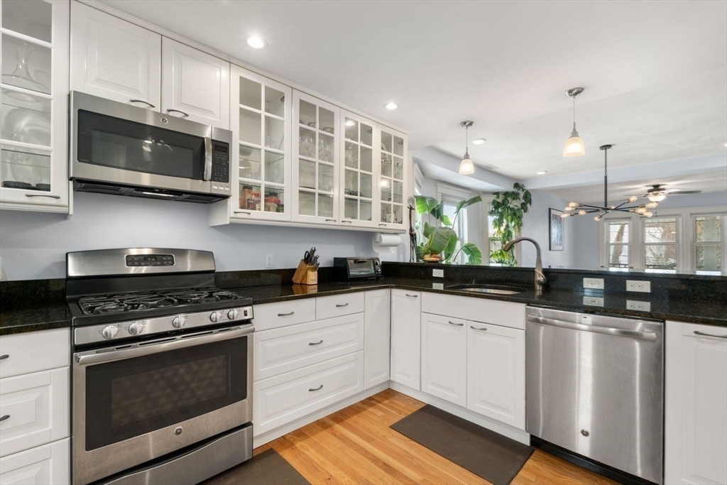 Kitchen with white cabinets, black countertops, stainless steel appliances, and a sink overlooking the dining area.