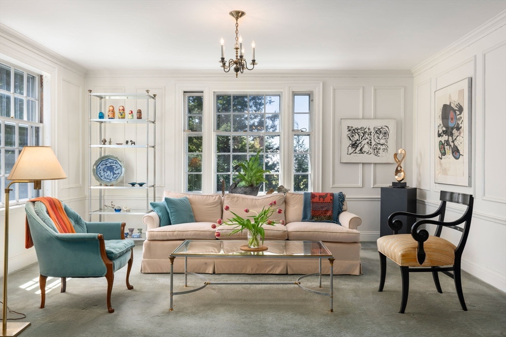 Living room with a beige sofa, teal armchair, glass coffee table, and tall sunlit windows.