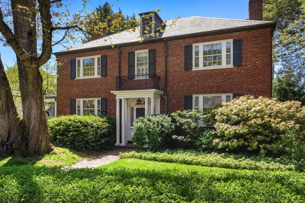 Two-story red brick house with a columned entry, black shutters, and landscaped front yard.