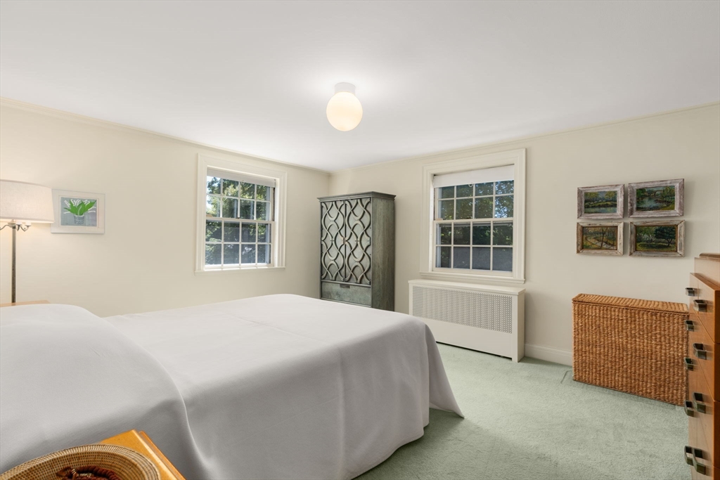 Bedroom with a large white-covered bed, two windows, and a patterned cabinet.