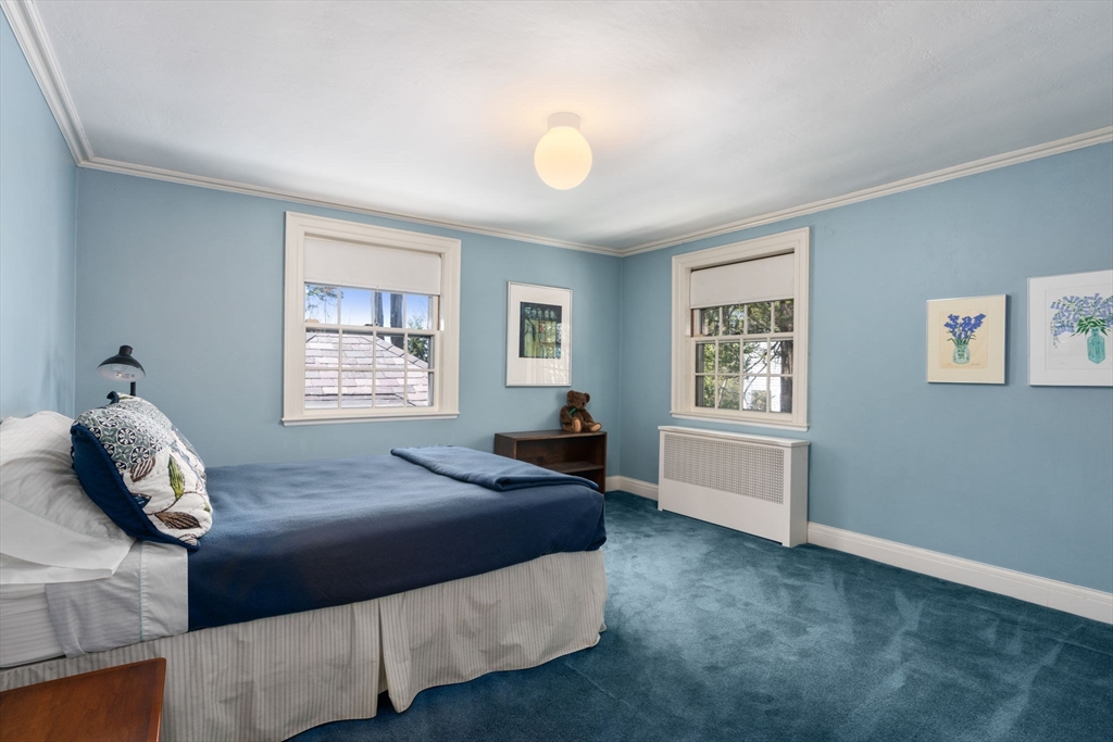 Bedroom with pale blue walls, blue carpet, a navy-covered bed, and two windows.