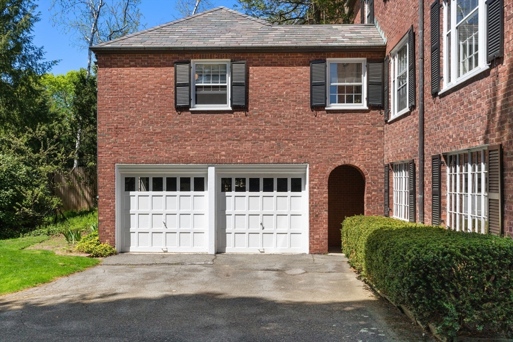 Red-brick house exterior with two white garage doors, black shutters, and an arched entry.