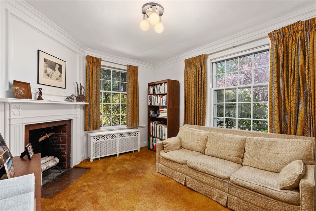 Living room with a cream sofa, white fireplace, and tall windows overlooking spring blossoms.