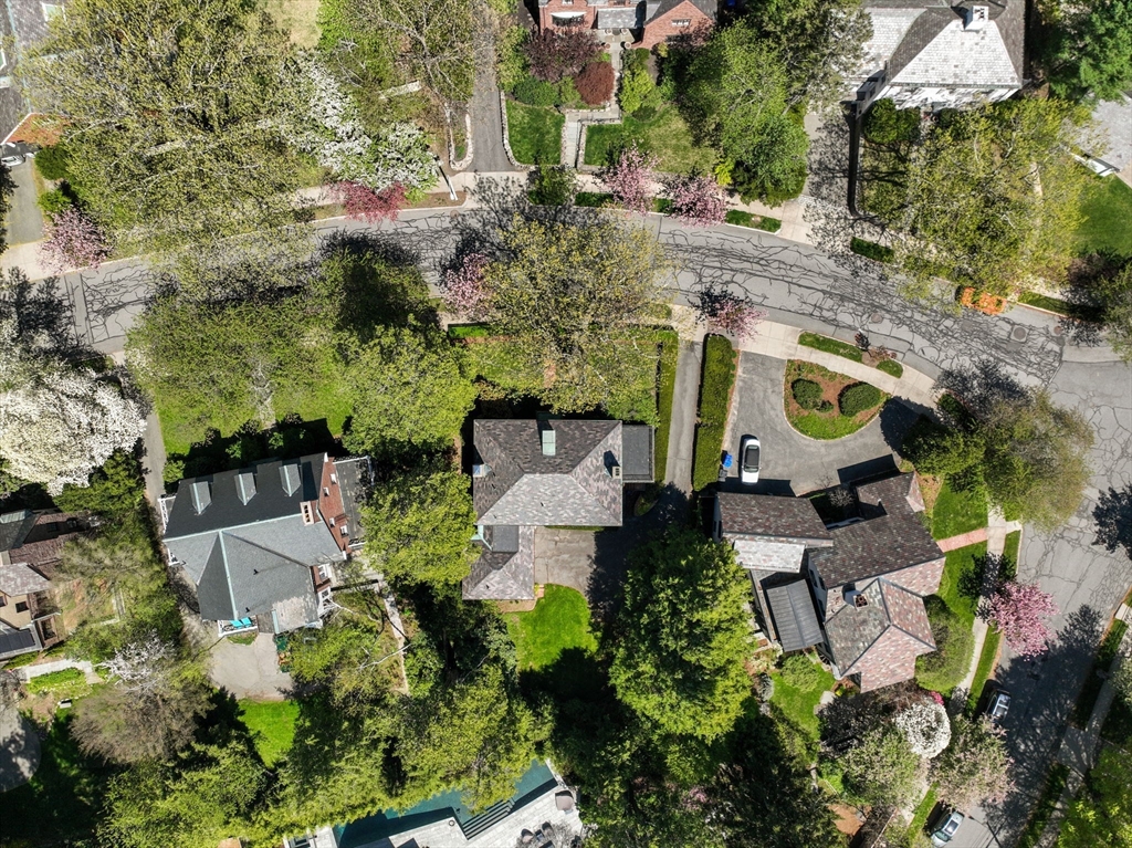 Aerial view of a detached house with a driveway and landscaped lawn amid flowering trees.