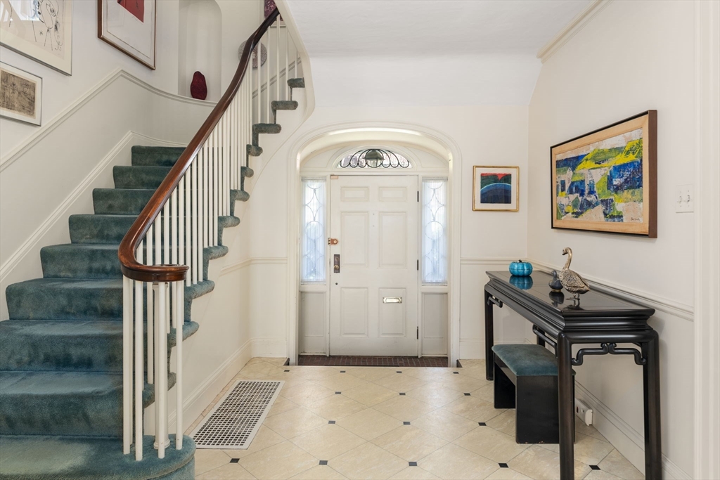 Entry foyer with a curved teal-carpeted staircase, arched front doorway, and patterned tile floor.