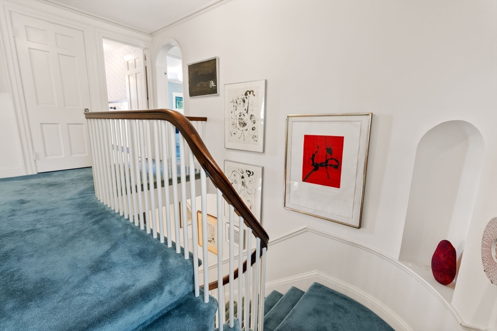 Carpeted staircase with a curved wood handrail, white balusters, framed artwork, and an arched wall niche.