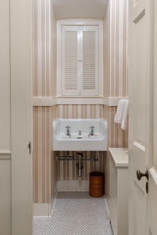 Narrow bathroom with striped wallpaper, a white sink, shuttered window, and hexagonal tile floor.