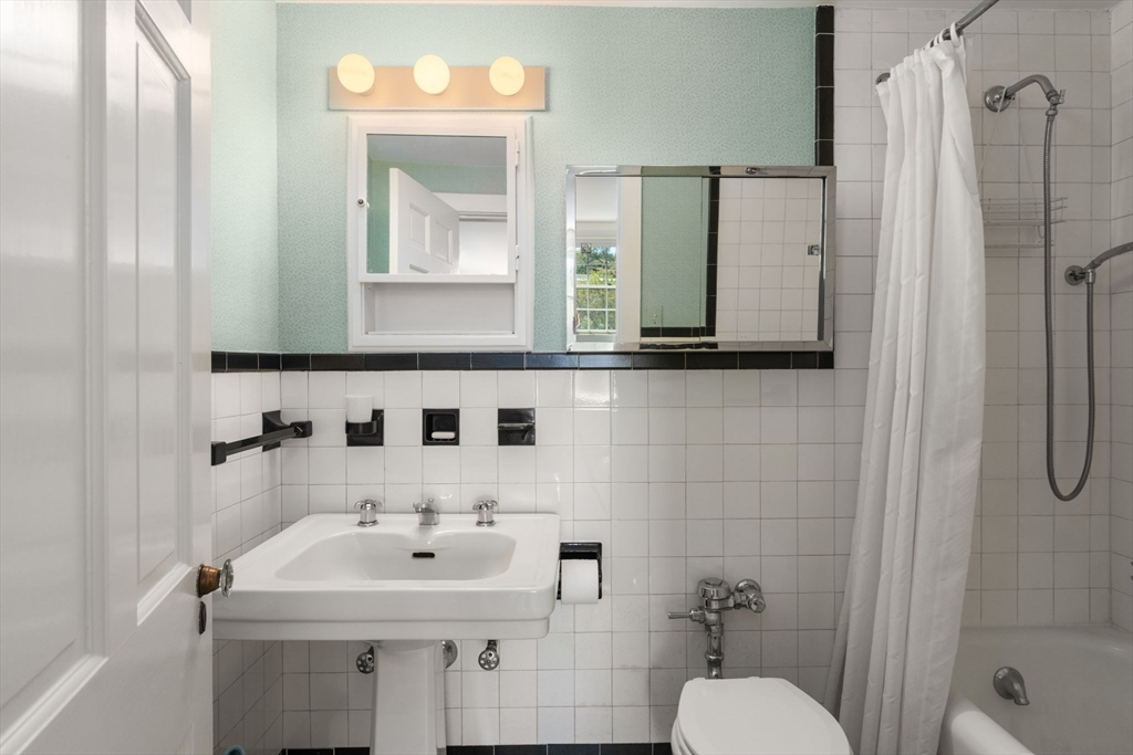 Bathroom with pedestal sink, tiled walls, mirrored cabinet, and curtained bathtub.