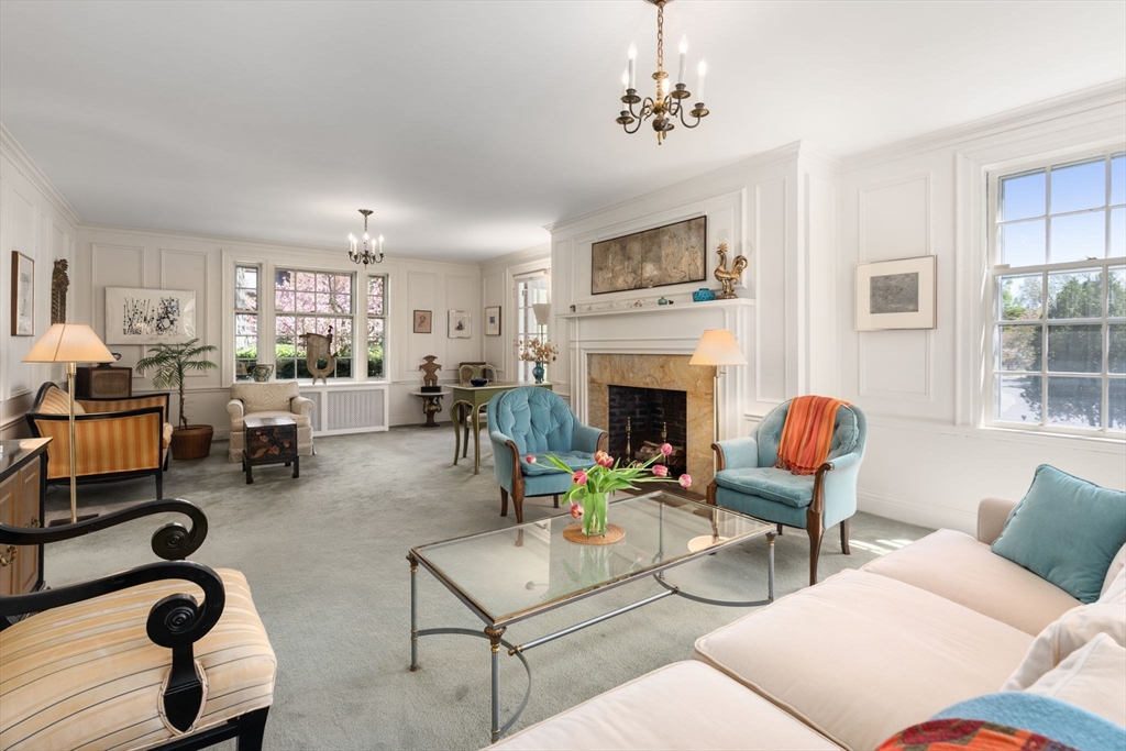 Living room with a stone fireplace, blue armchairs, and large windows overlooking flowering trees.