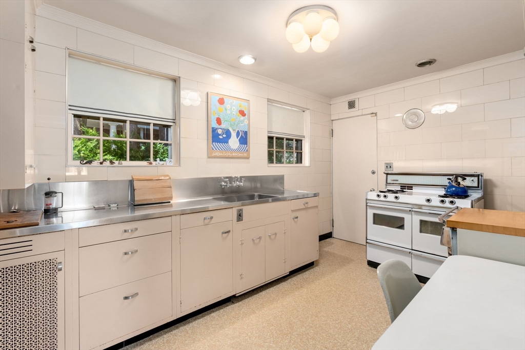 Kitchen with stainless steel counters, white cabinetry, two windows, and a large range.