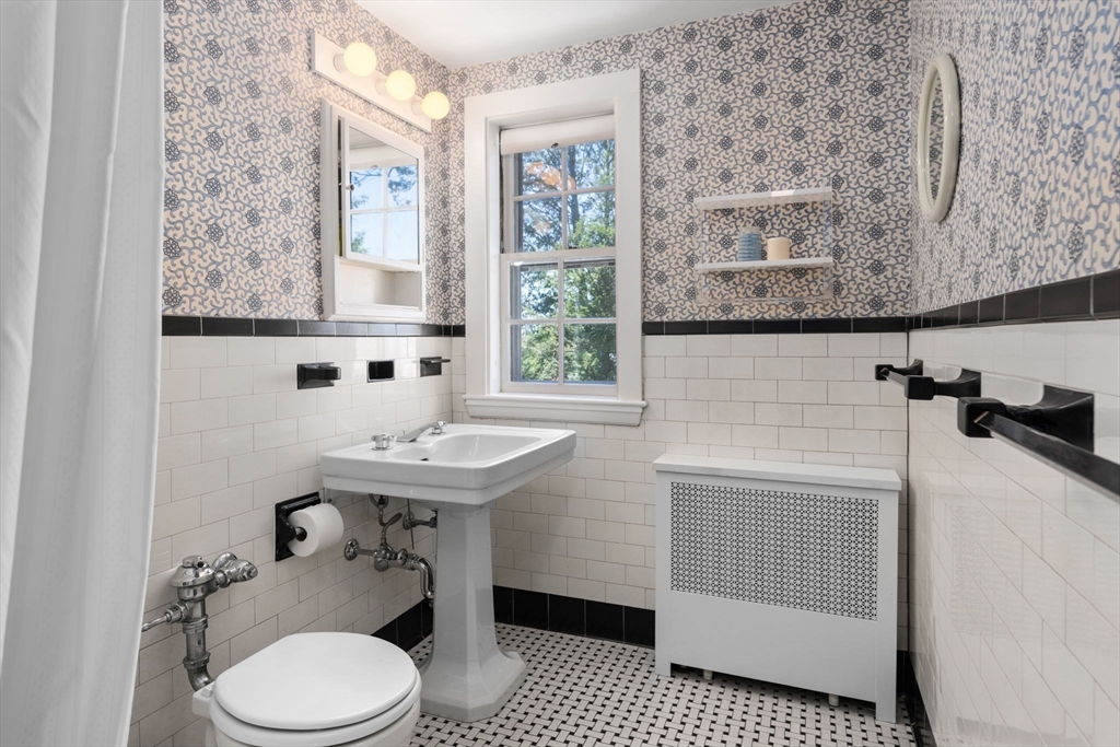 Bathroom with a pedestal sink, patterned wallpaper, subway tile, and mosaic flooring.