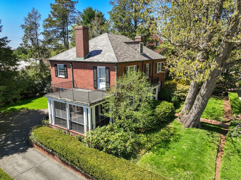 Red-brick home with a gray shingle roof, balcony, screened porch, and landscaped lawn.