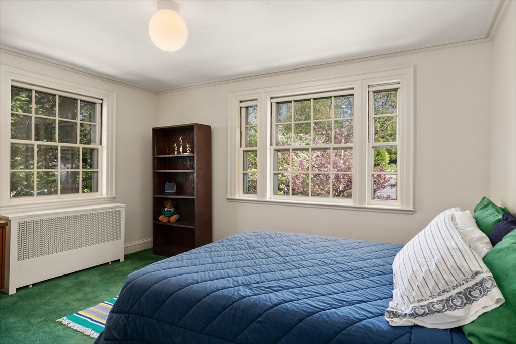 Bedroom with a blue-covered bed, green carpet, and large windows overlooking flowering trees.