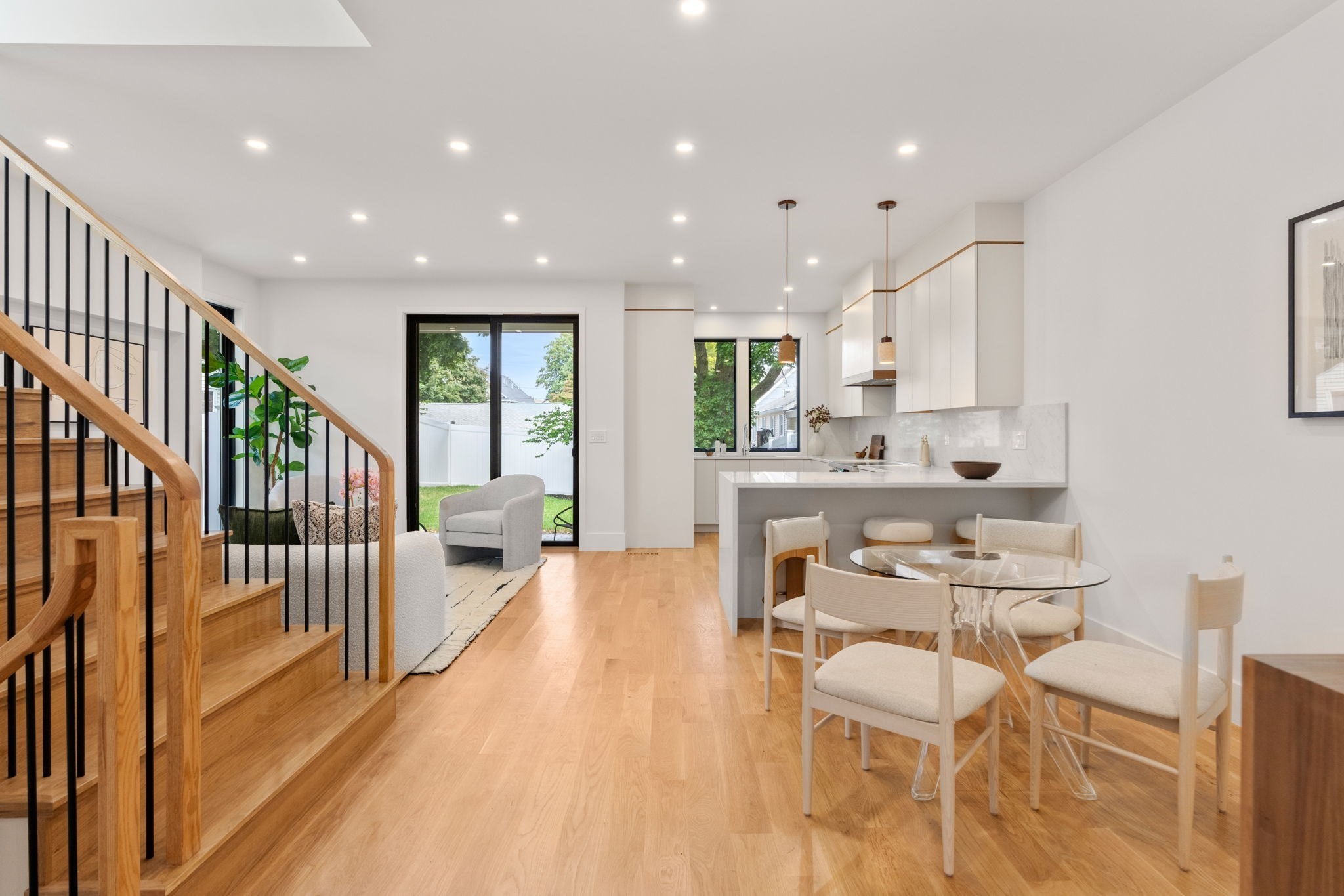 Open-plan kitchen and dining area with a glass table, wood staircase, and views of a fenced yard.