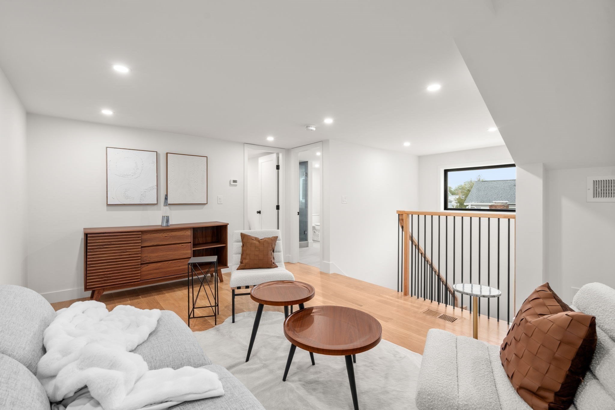 Bright living room with white sofas, round wood coffee tables, and a railing around the stairwell.