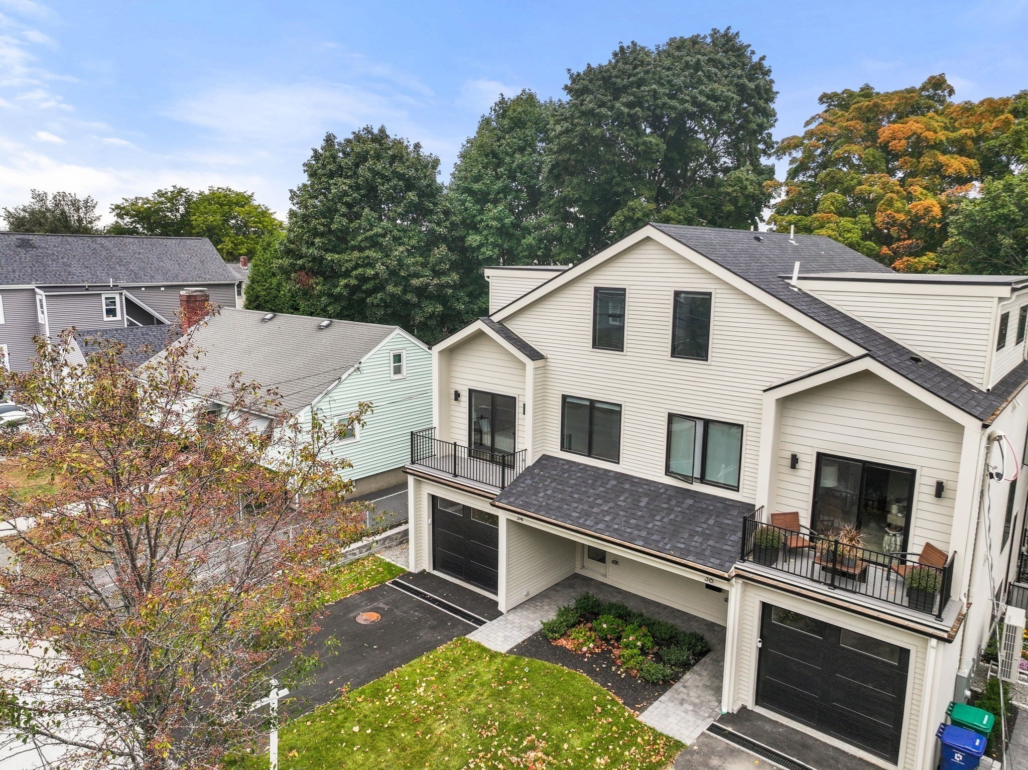 White-sided home with two dark garage doors, balconies, and autumn trees viewed from above.