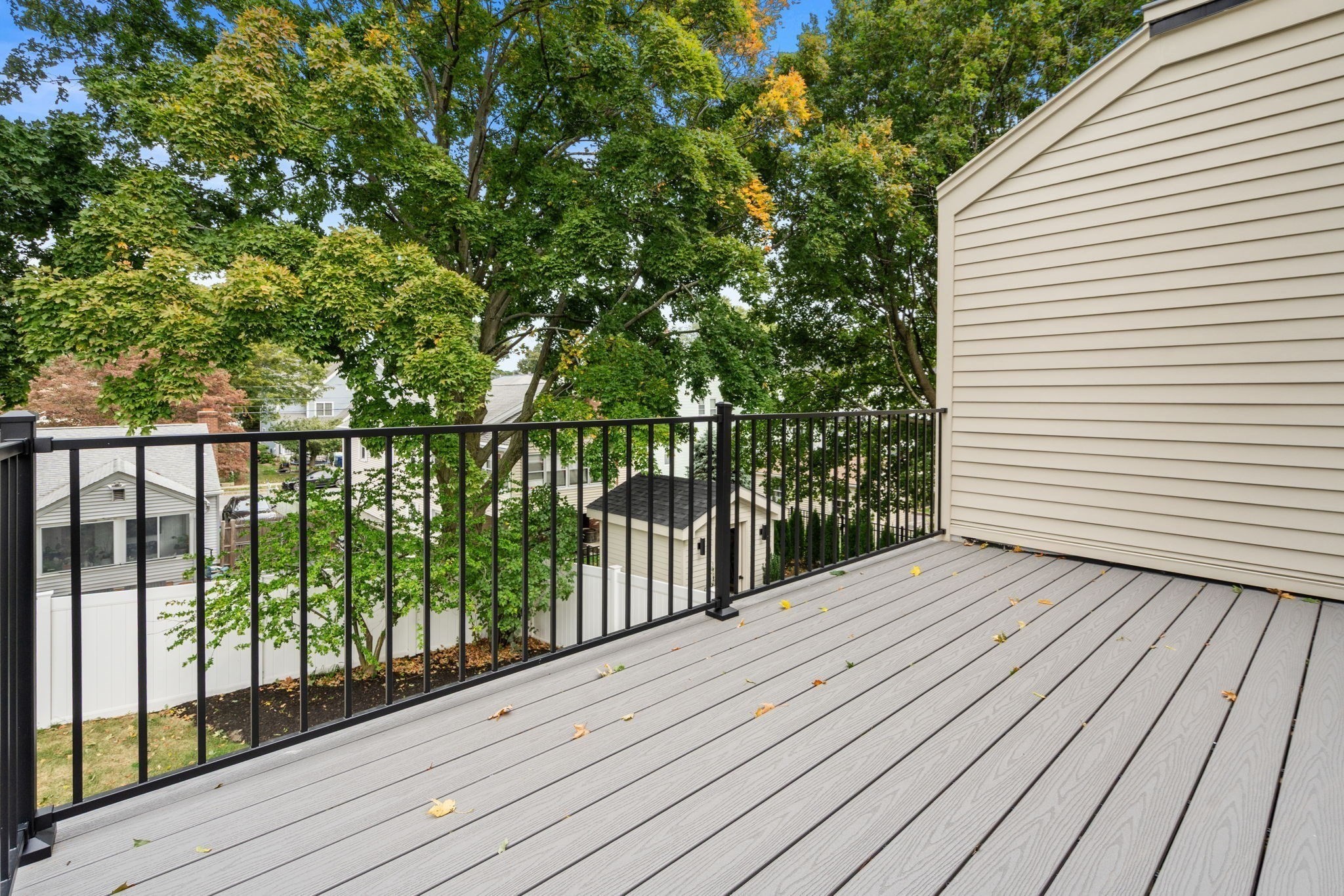 Elevated gray deck with black railings overlooking leafy trees and neighboring homes.