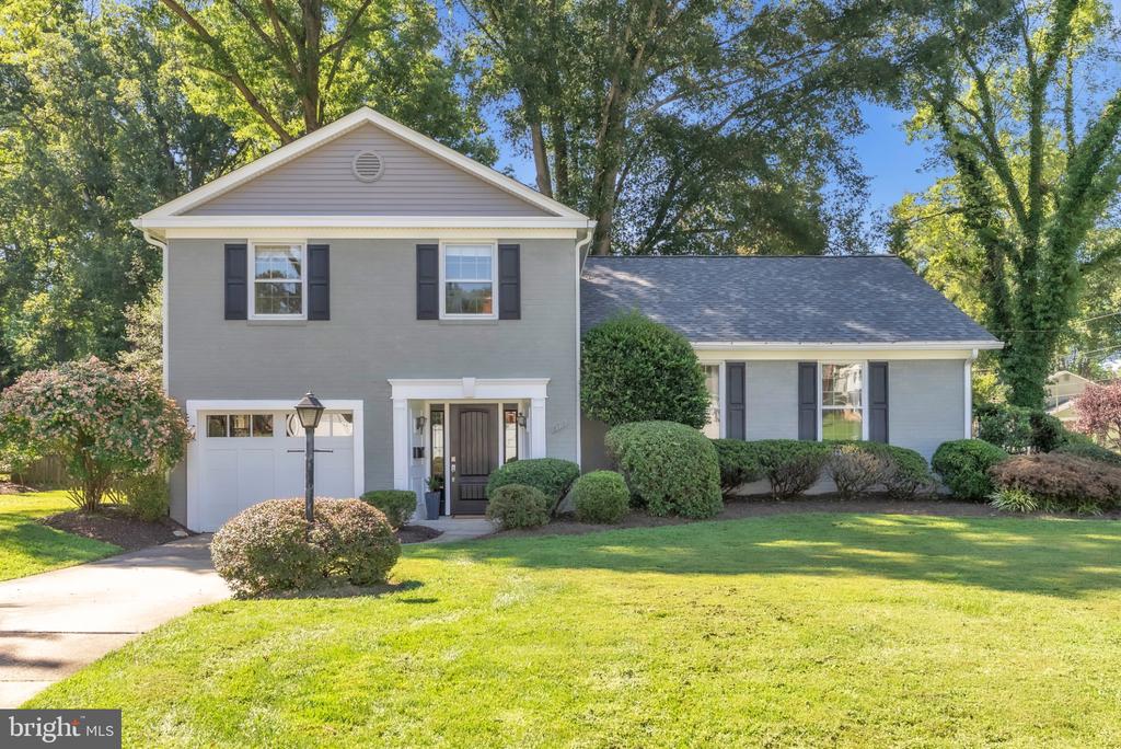 Gray two-story house with an attached garage, landscaped front yard, and mature trees.