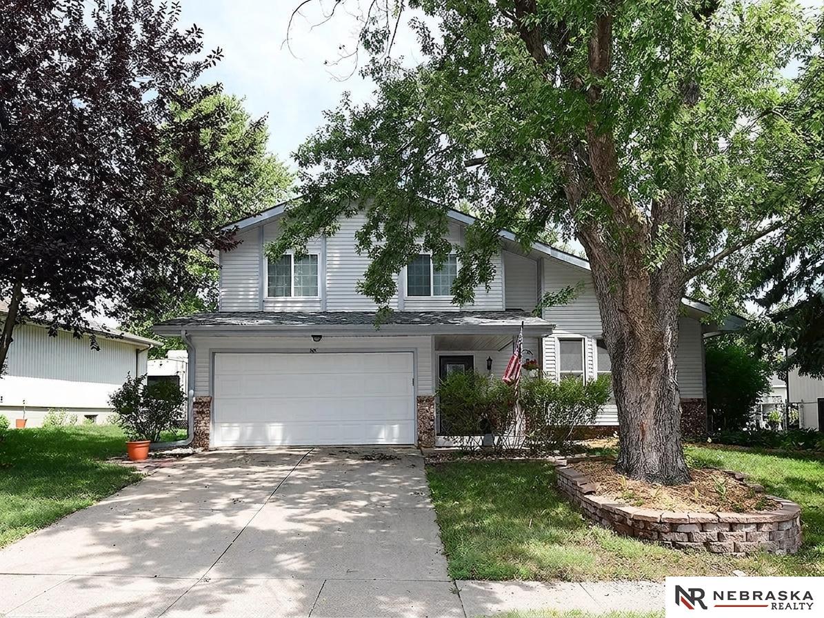 Two-story gray house with an attached double garage, driveway, and mature trees.