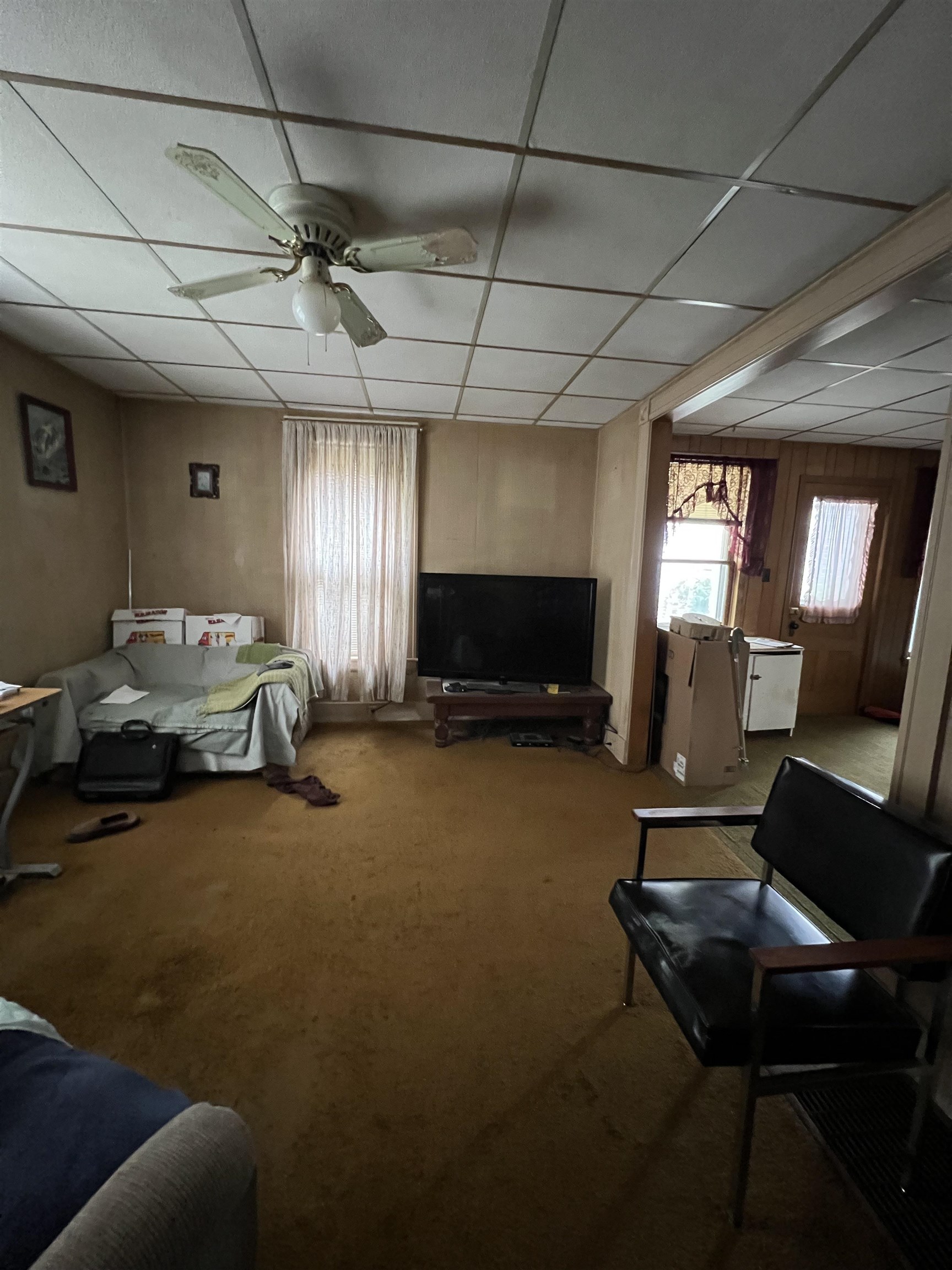 Living room with tan carpet, a ceiling fan, sofa, television, and an adjoining entry area.