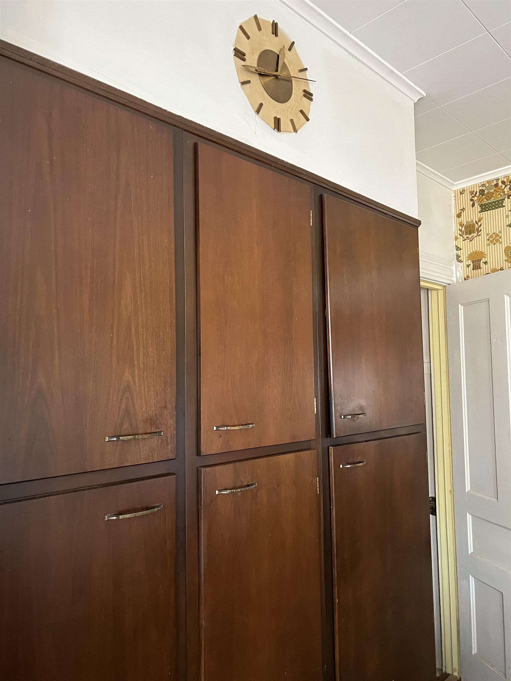 Dark wood built-in cabinets with drawers, a wooden wall clock above, and a white paneled door.