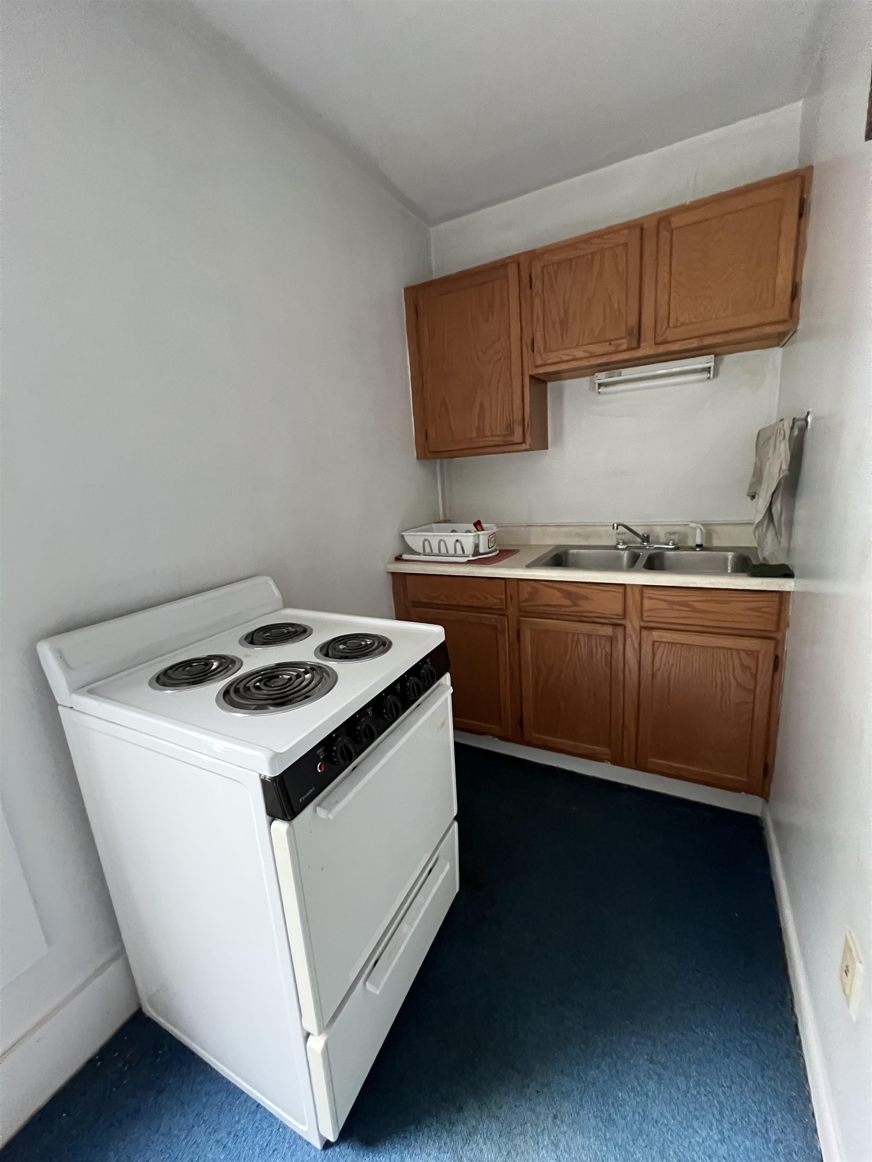Narrow kitchen with a white electric range, wood cabinets, and a double-basin sink.