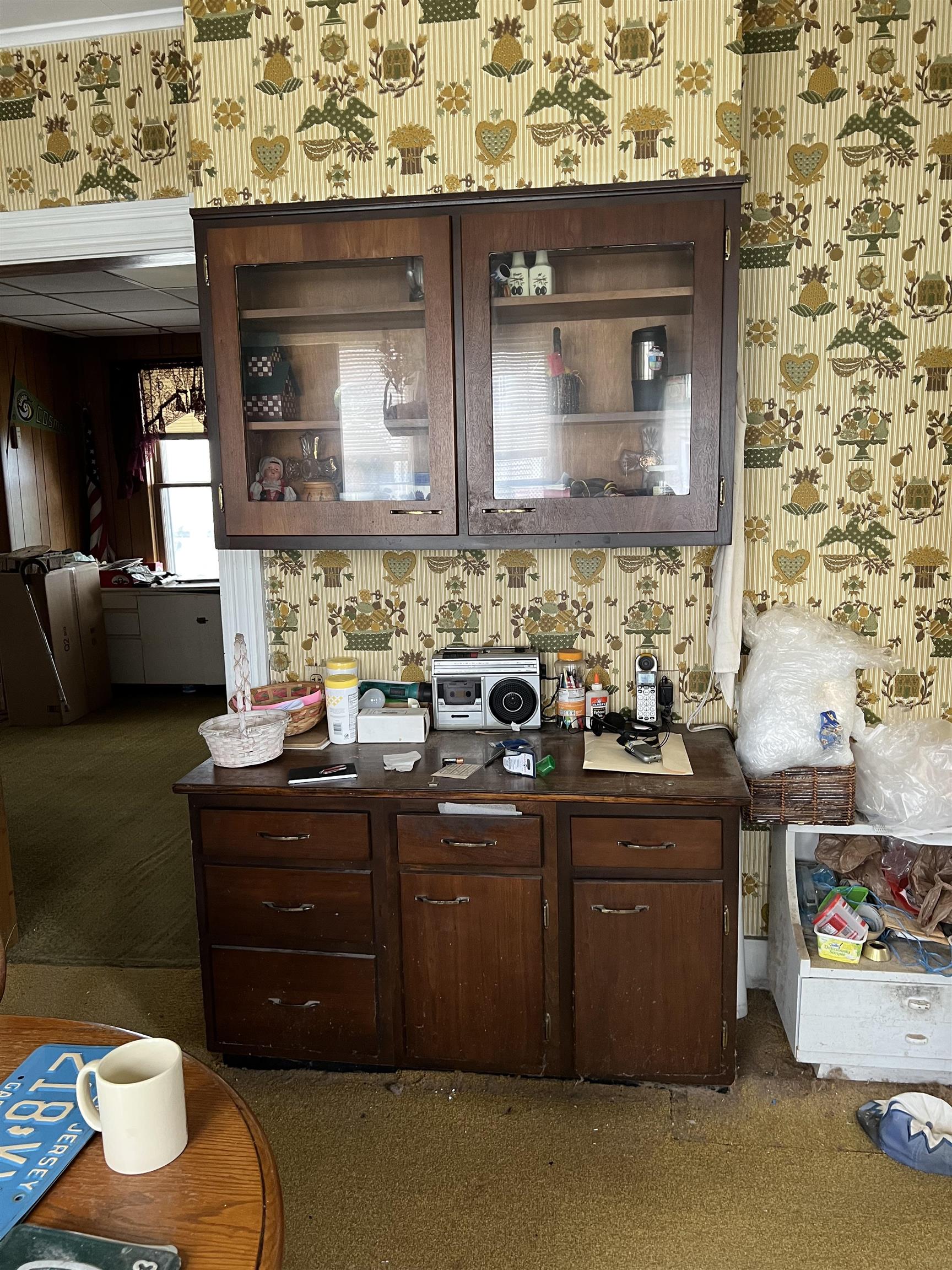 Room with a dark wood china cabinet and buffet against ornate yellow patterned wallpaper.