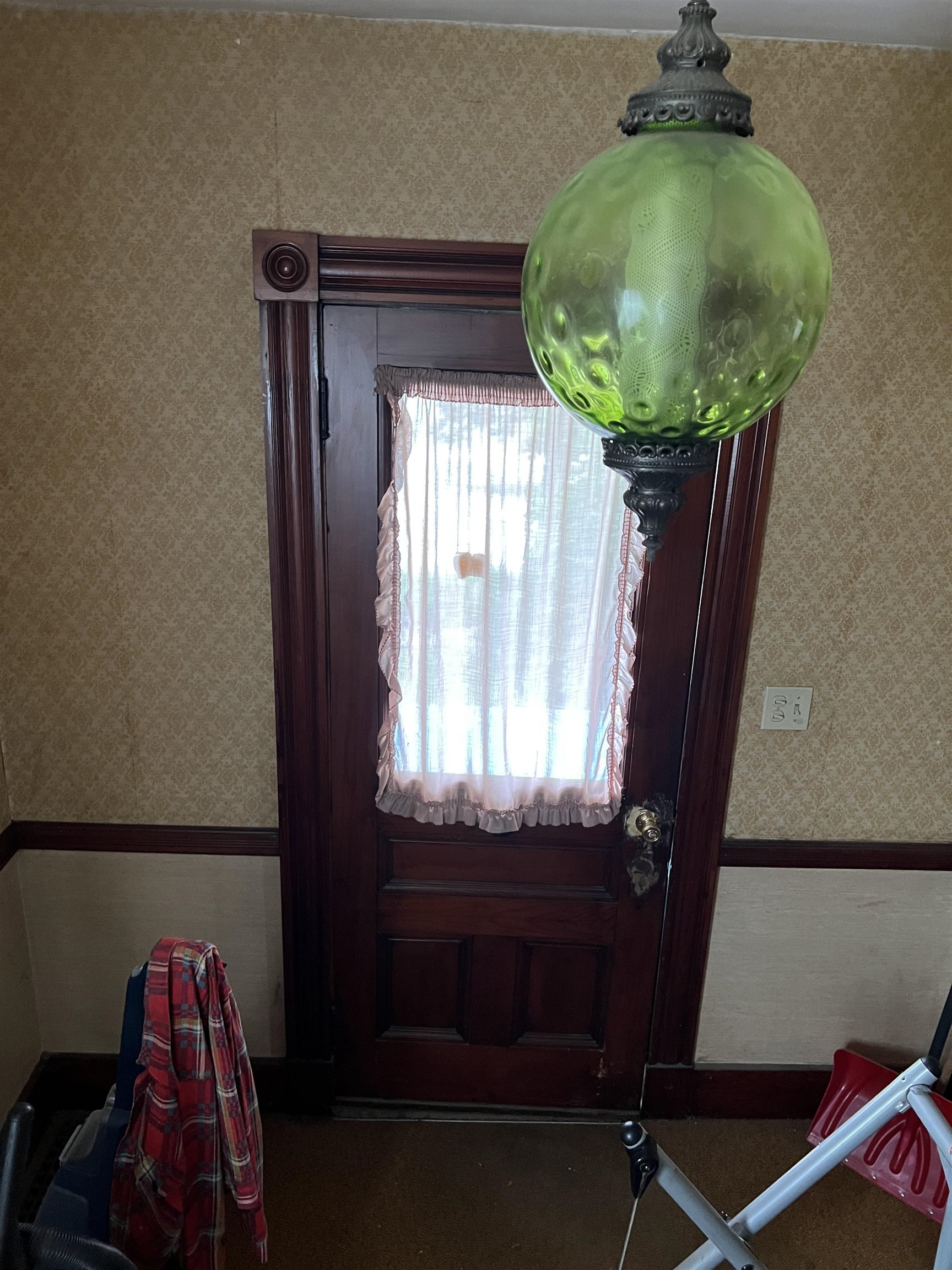 Dark wood entry door with a curtained window beneath a large green glass pendant light.