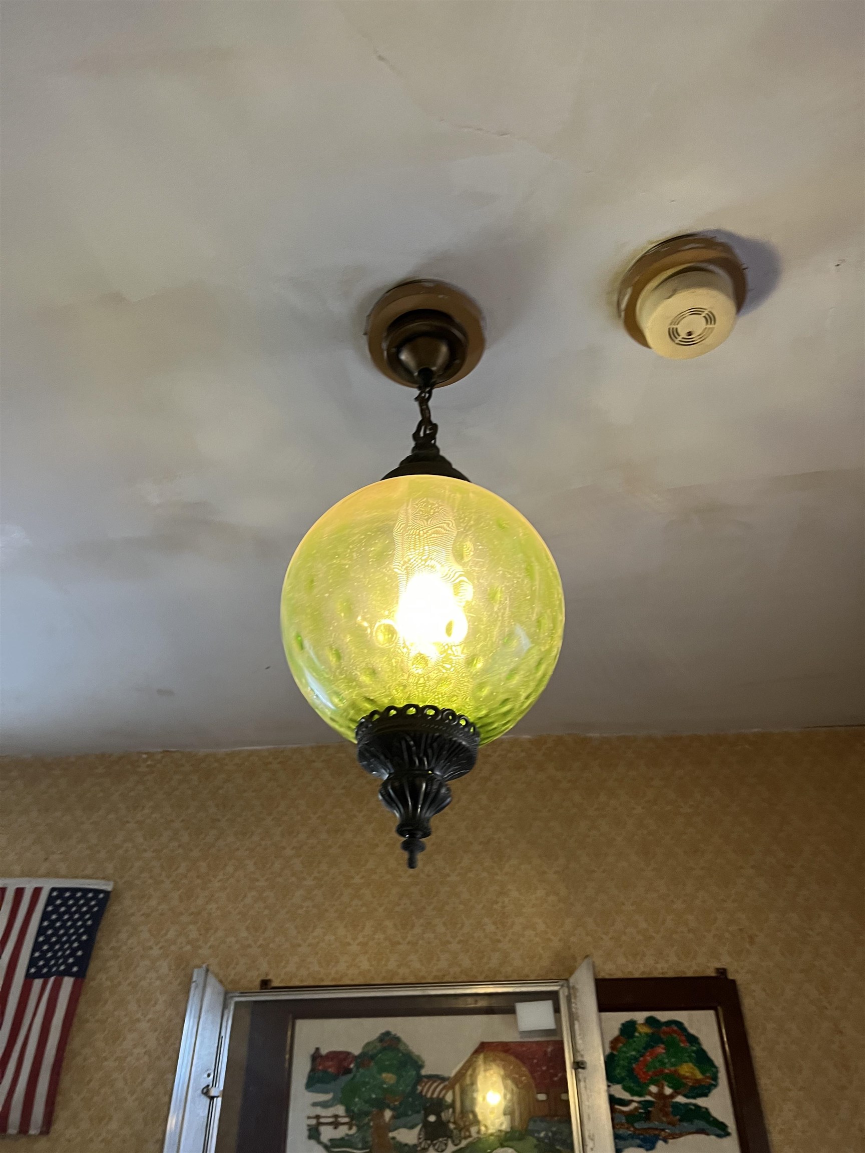 Green glass pendant light hanging from the ceiling above framed artwork and patterned wallpaper.