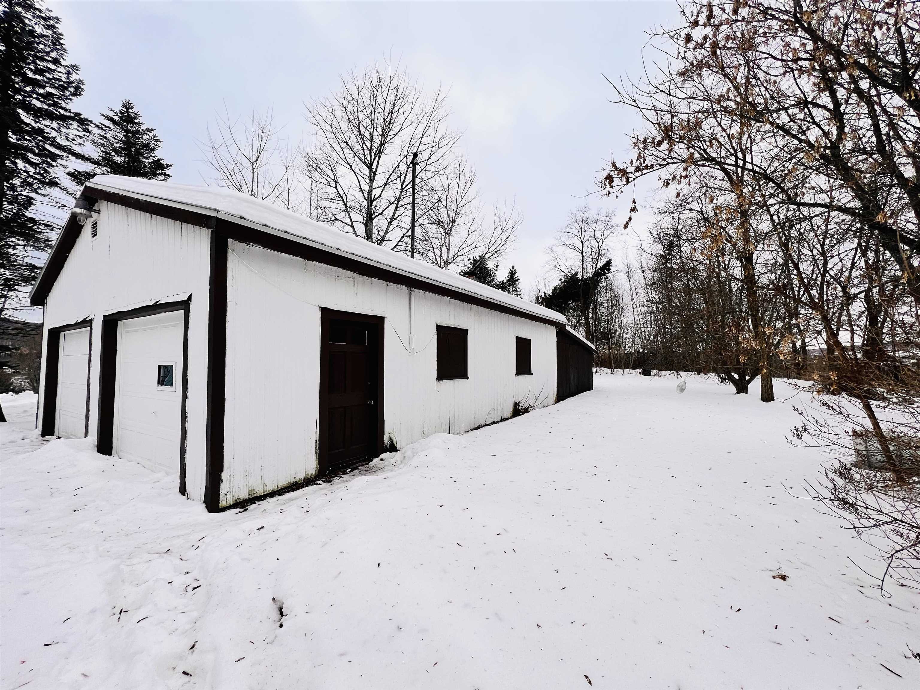 White detached garage with two overhead doors and dark trim in a snowy yard.