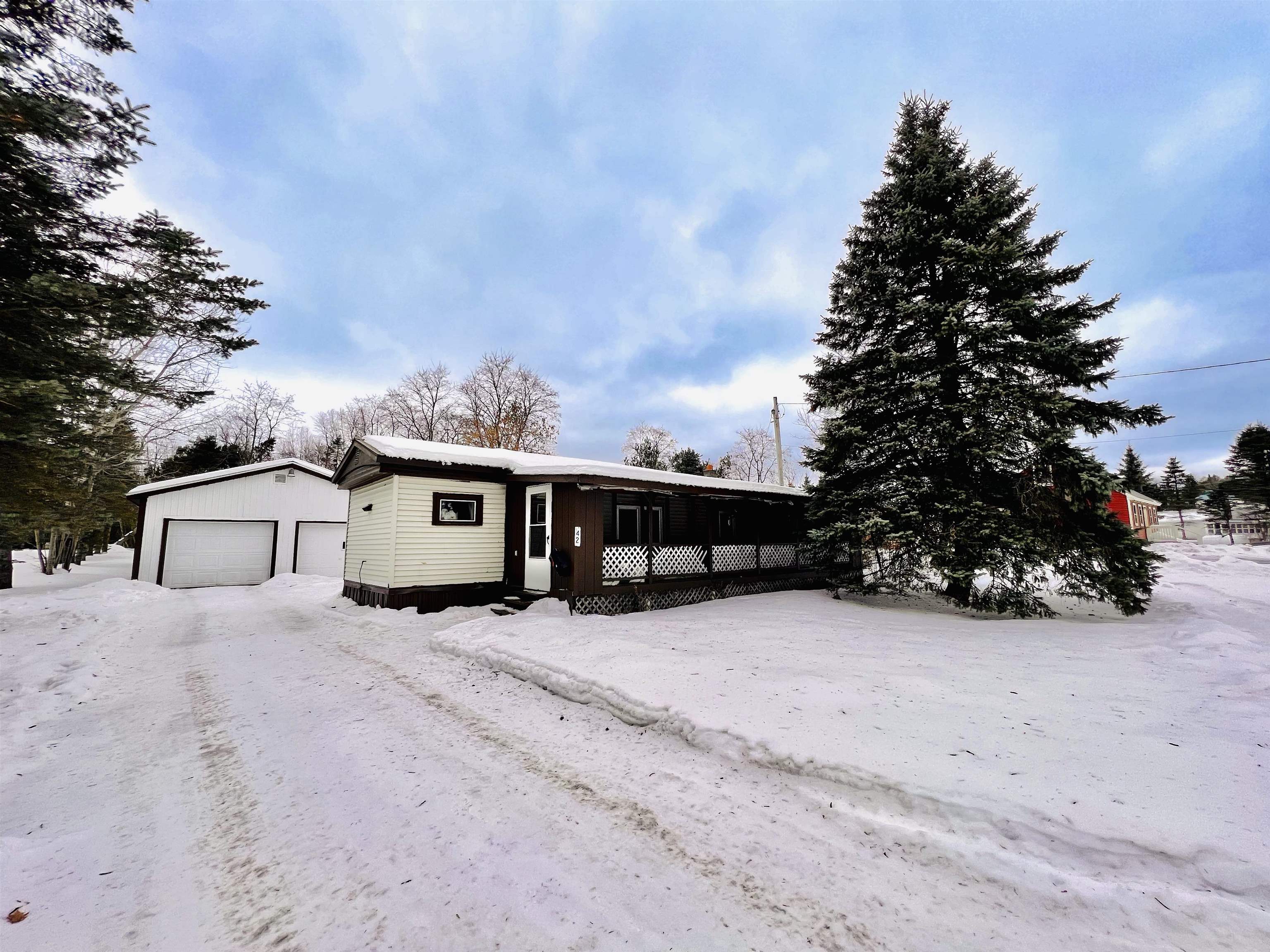 Single-story home with a covered porch and attached garage, surrounded by snow and a large evergreen.