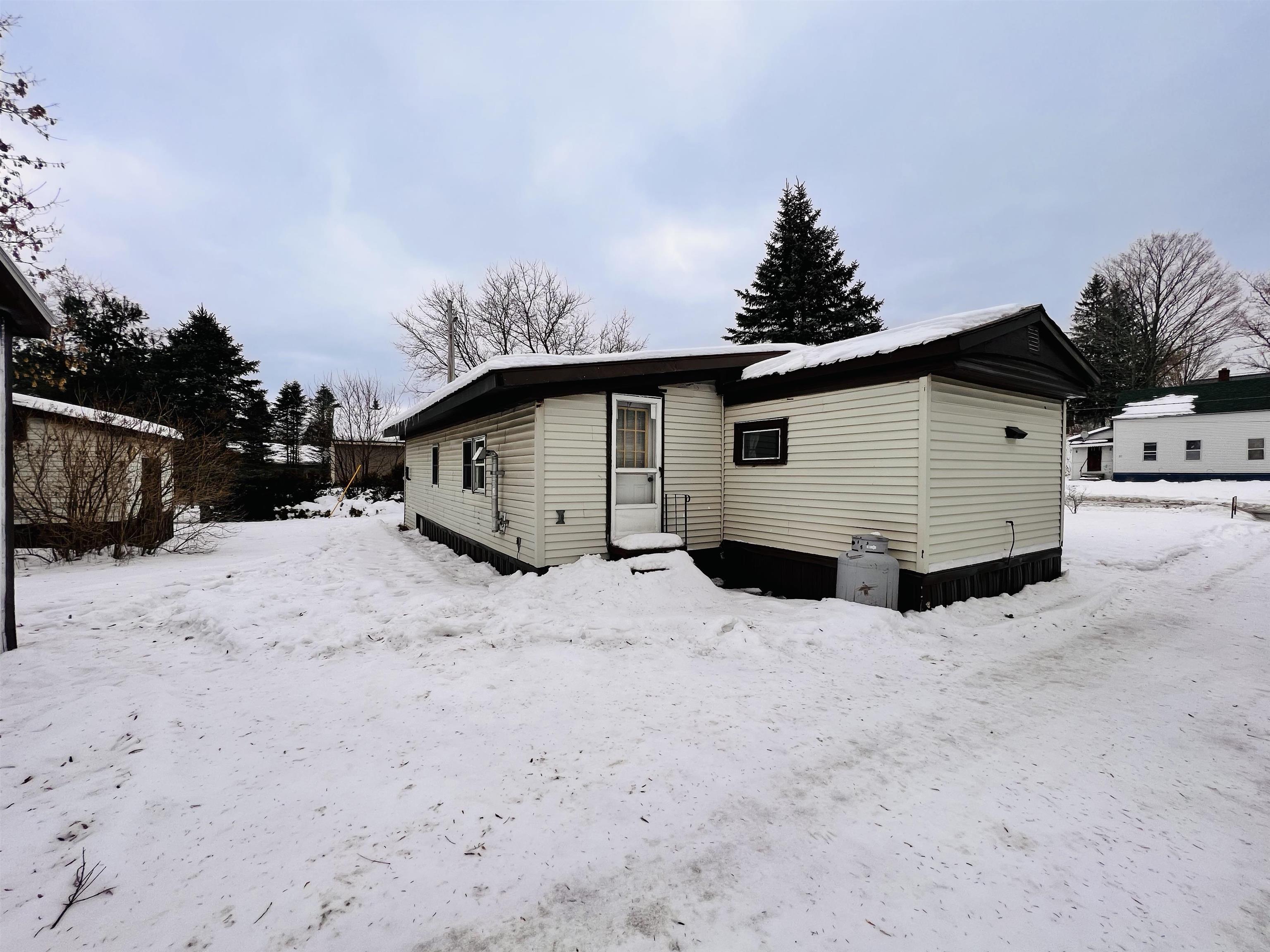 Single-story light-sided home with a low-pitched roof in a snow-covered yard.