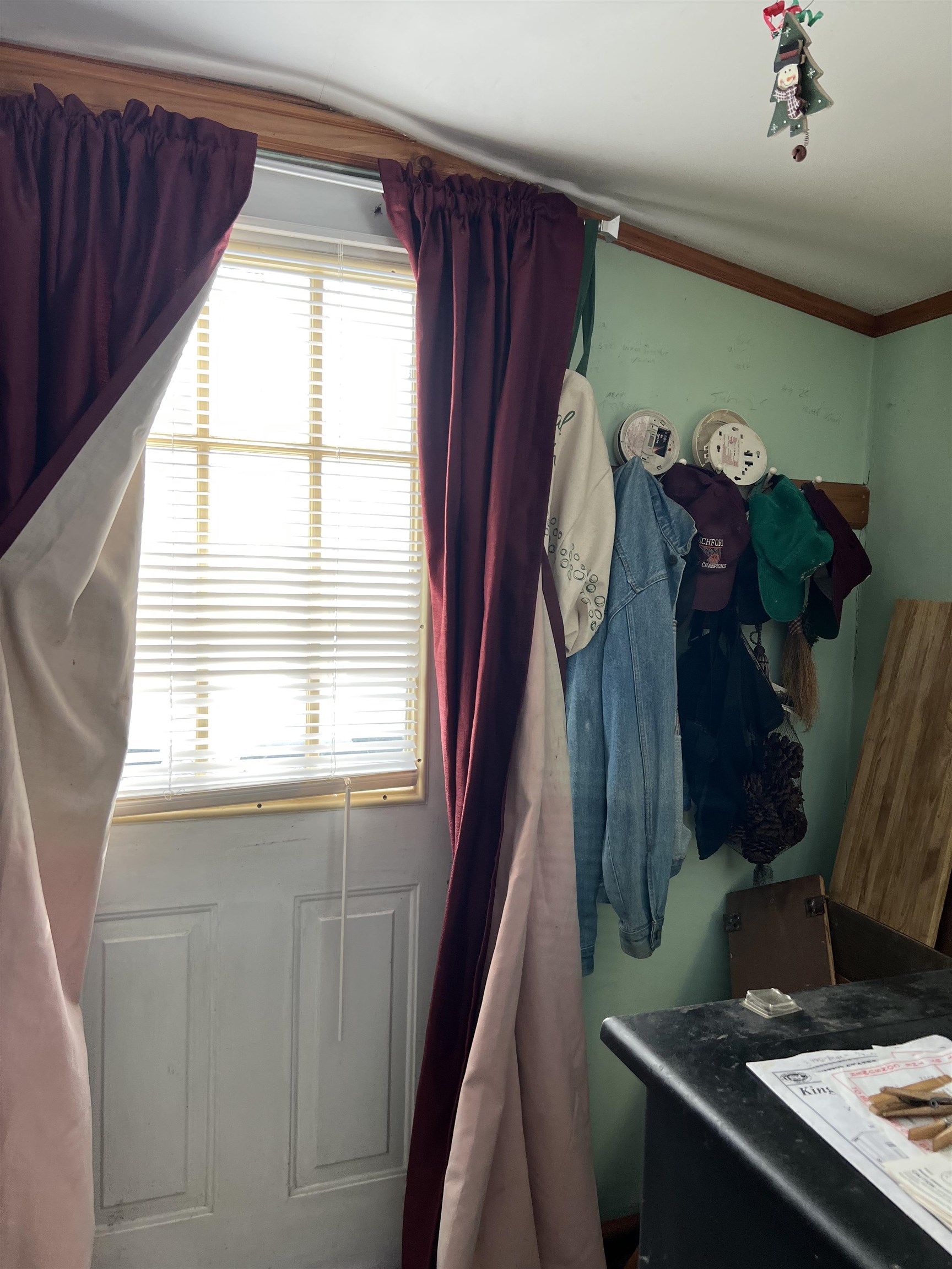 Entryway with a windowed white door, burgundy curtains, and coats and hats hanging on a mint-green wall.