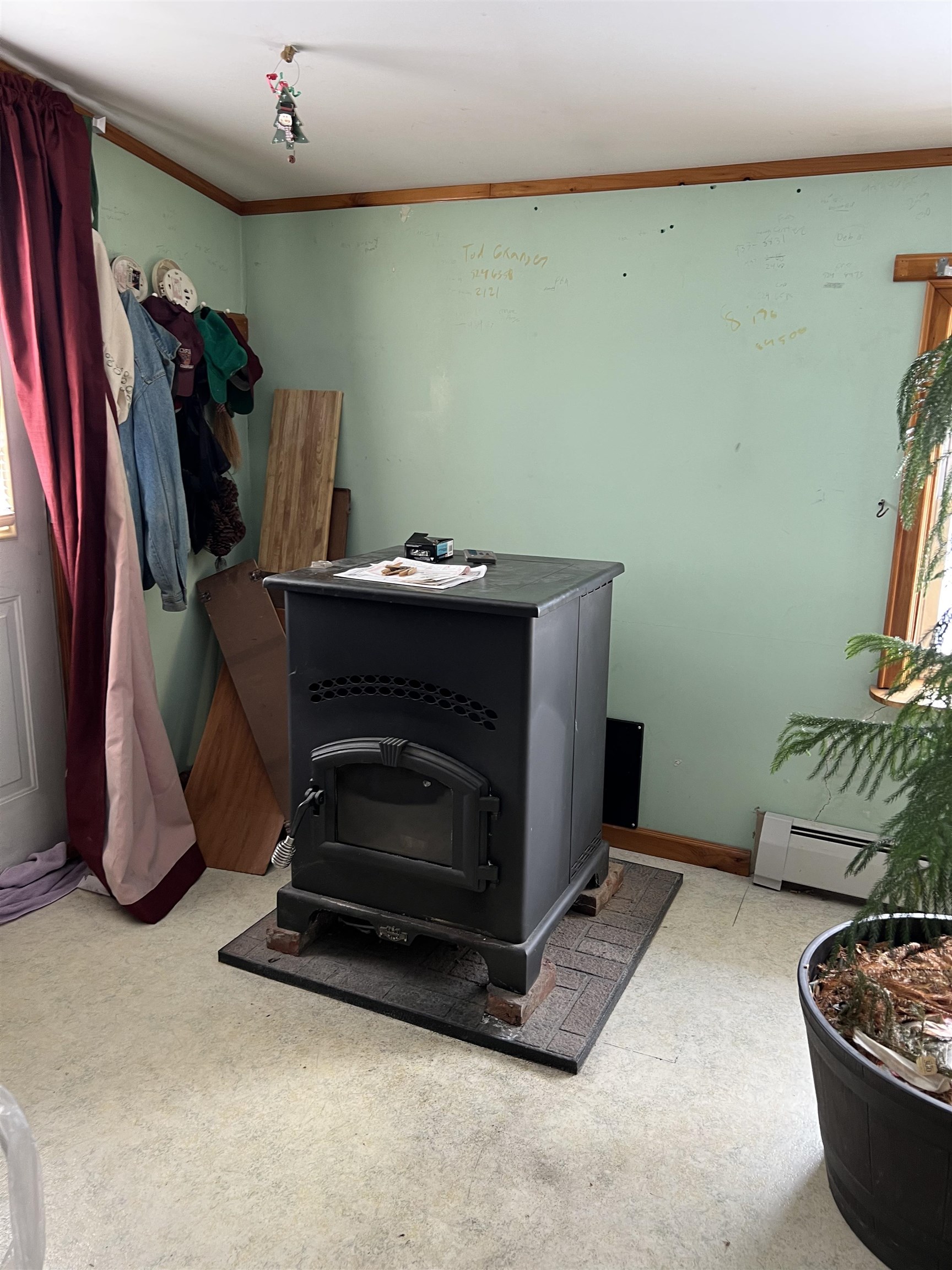 Black freestanding wood stove on a tiled hearth in a room with hanging coats and a potted evergreen.